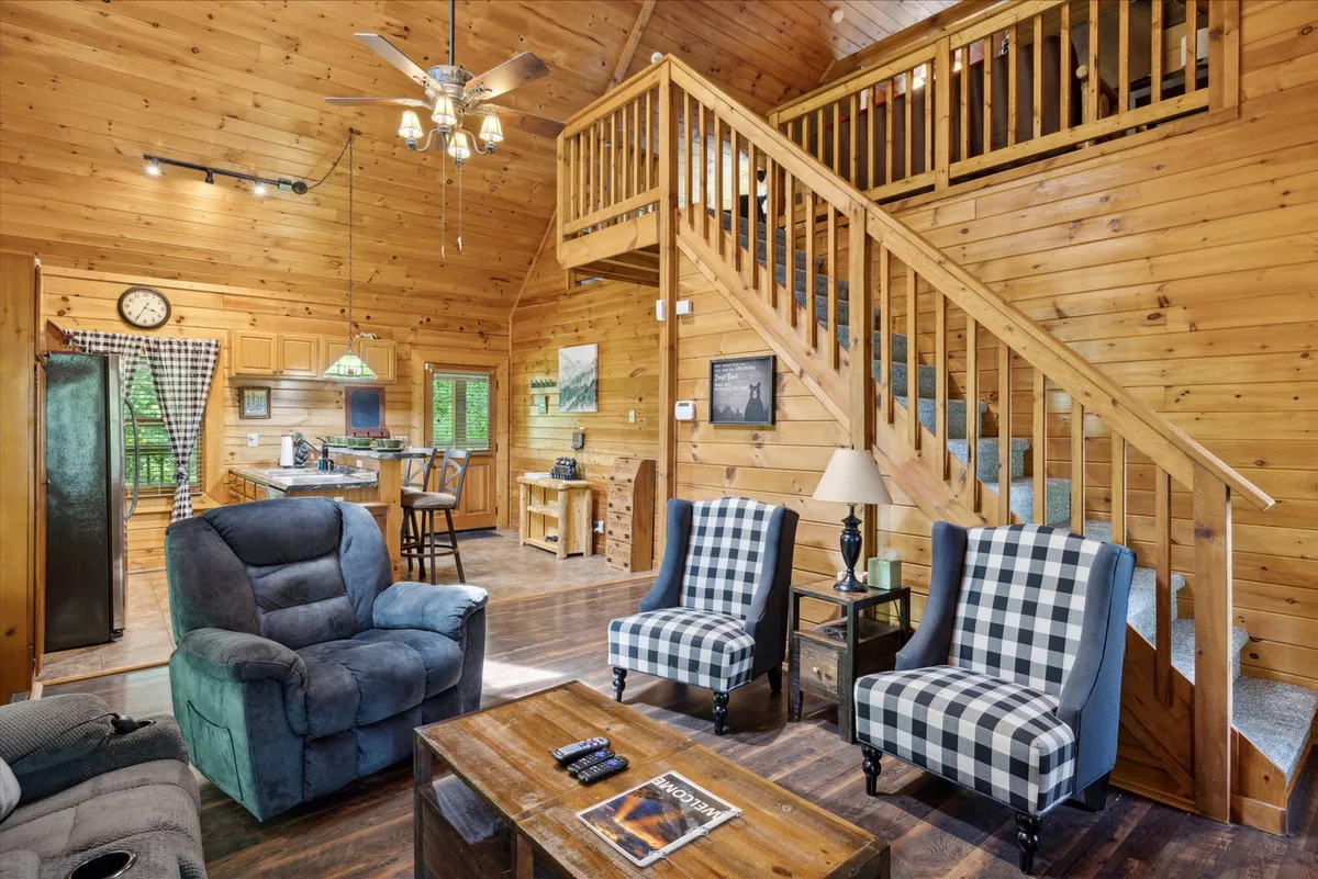 This image provides a broader perspective of the interior, showing the kitchen area from afar alongside a wooden table with blue chairs and a staircase leading upstairs. The setup suggests an easy flow between cooking, dining, and other communal activities, with the dining area seamlessly connected to the kitchen.