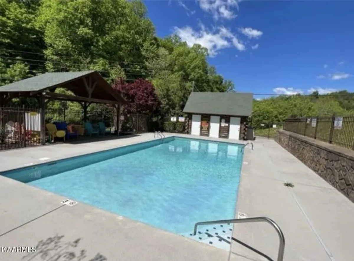 A spacious outdoor pool area featuring colorful sun loungers, a pool for swimming, and nearby changing rooms. The area is designed for relaxation and socializing, set within a landscaped environment that feels inviting and leisurely.