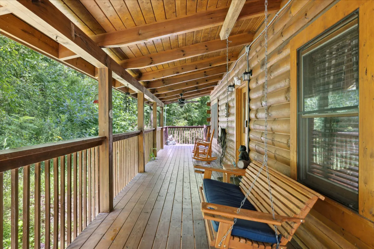 A cozy porch setting with wooden rocking chairs sits against the backdrop of log cabin walls and lush greenery. The space suggests leisurely mornings with coffee or evenings spent watching the stars, with the inviting natural surroundings creating a tranquil, private retreat.