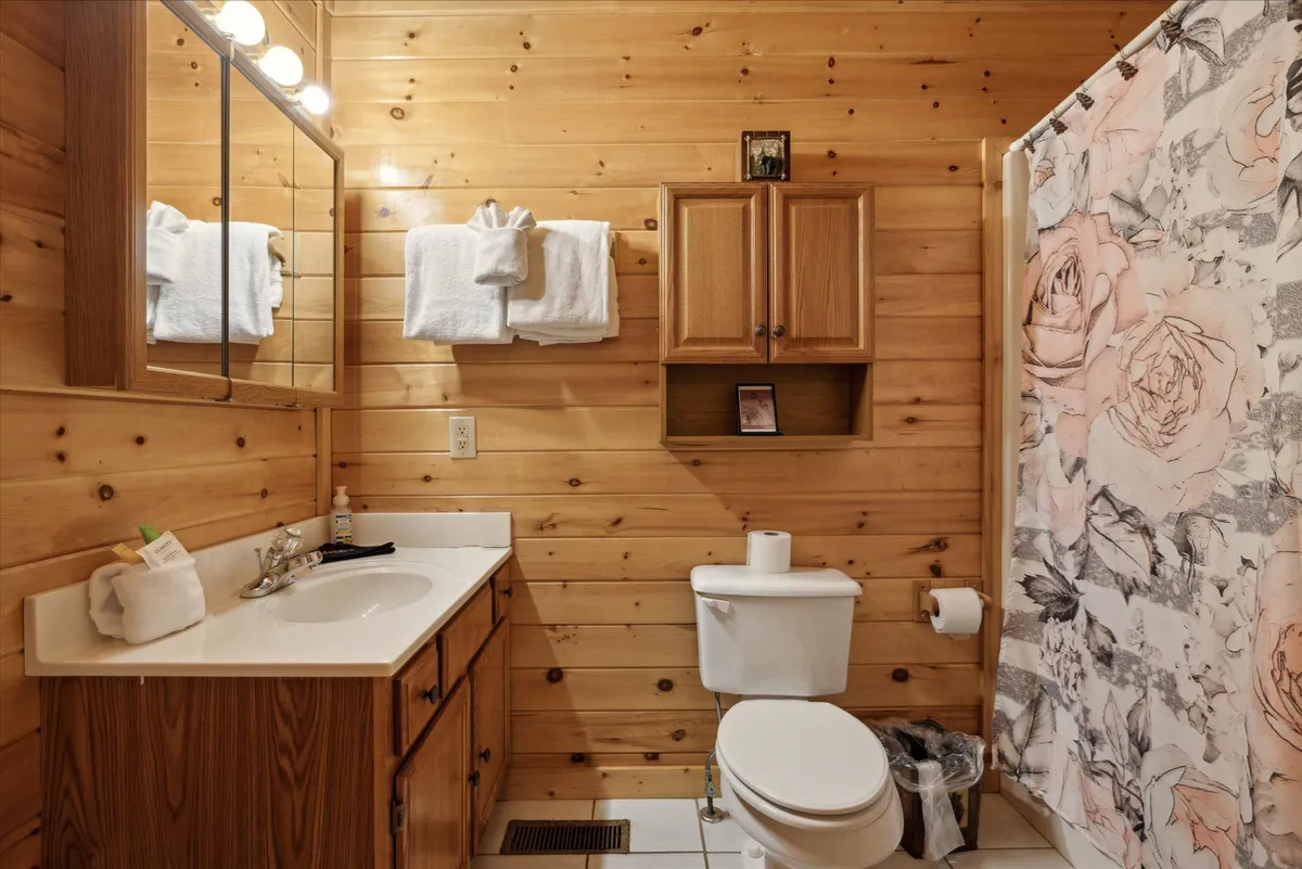 A tranquil bathroom with wooden paneling, a floral shower curtain, and a tidy sink with toiletries arranged for comfort and convenience. The overall mood is serene and calming, ideal for self-care routines.