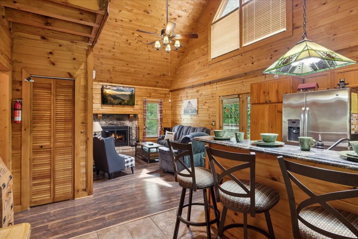 An open-concept space seamlessly integrating the living area, kitchen, and dining, with a fireplace, kitchen island, and large windows. The setting is cozy and welcoming, perfect for shared meals, entertaining, or lazy afternoons by the fire.