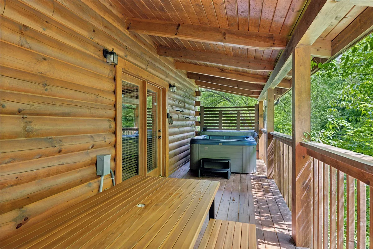 This image captures a tranquil outdoor setting featuring a private hot tub next to a rustic log cabin structure. A wooden table is nearby, perfect for outdoor dining, and dense trees surround the scene, emphasizing the sense of privacy and immersion in nature. The overall mood is peaceful and intimate, ideal for couples seeking relaxation.